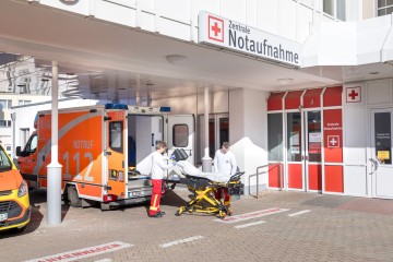 Außenbereich der Notaufnahme eines Krankenhauses; zwei Sanitäter bereiten eine Krankentrage vor
