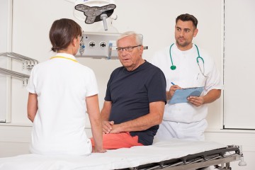 zwei Ärzte am Krankenbett im Gespräch mit einem Patienten