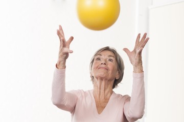 Eine ältere Frau wirft einen Ball in die Höhe.