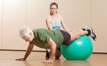 Das BIld zeigt einen älteren Patienten der mit einem Gymnastikball Rückenübungen macht.