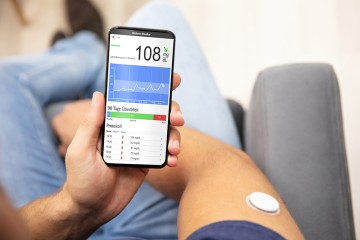 ein Mensch hält ein Handy, eine App mit Diabetiker-Tagebuch ist geöffnet