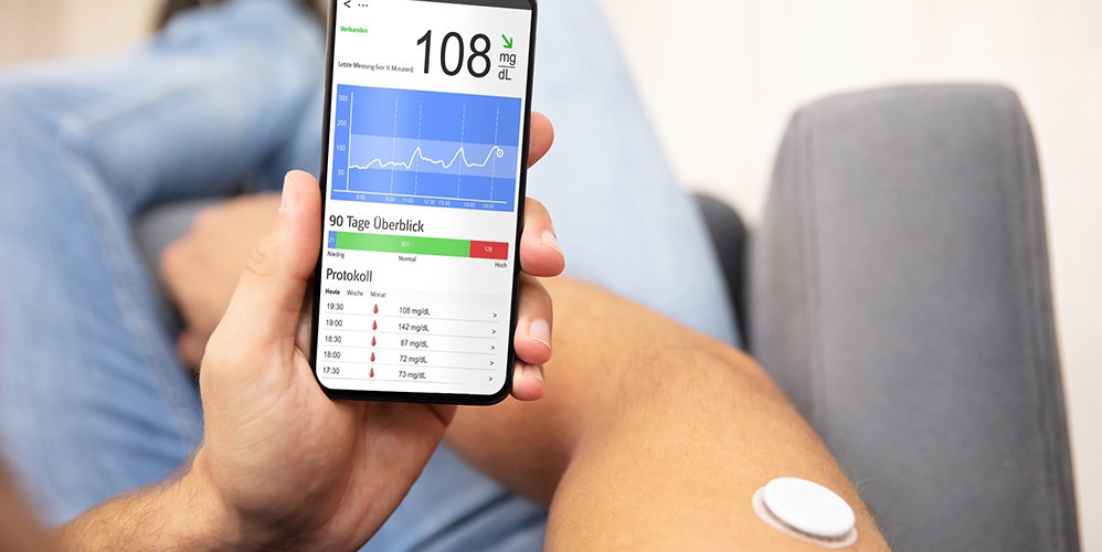 ein Mensch hält ein Handy, eine App mit Diabetiker-Tagebuch ist geöffnet