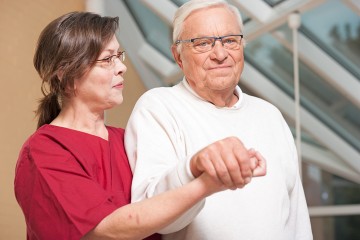 Ein Pflegebedürftiger wird von einer Pflegerin gestützt.