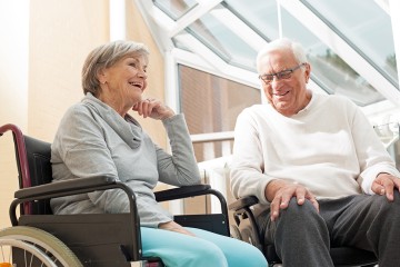 Zwei Pflegebedürftige sitzen im Rollstuhl und unterhalten sich.