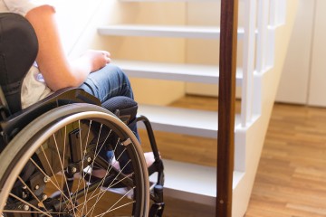 angeschnittene Person im Rollstuhl vor einer Treppe