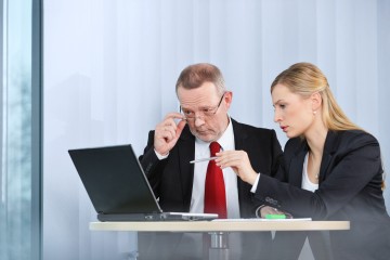 ein älterer Mann und eine junge Frau schauen gemeinsam auf einen Laptop