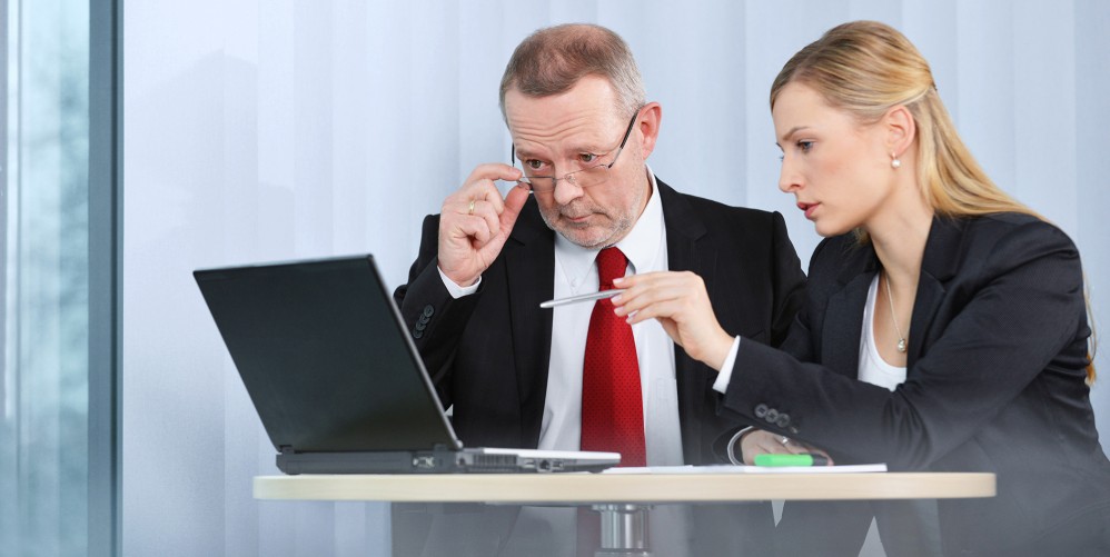 ein älterer Mann und eine junge Frau schauen gemeinsam auf einen Laptop