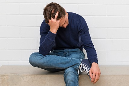 Ein junger Mann sitzt auf einer Bank und stützt den Kopf mit einer Hand.