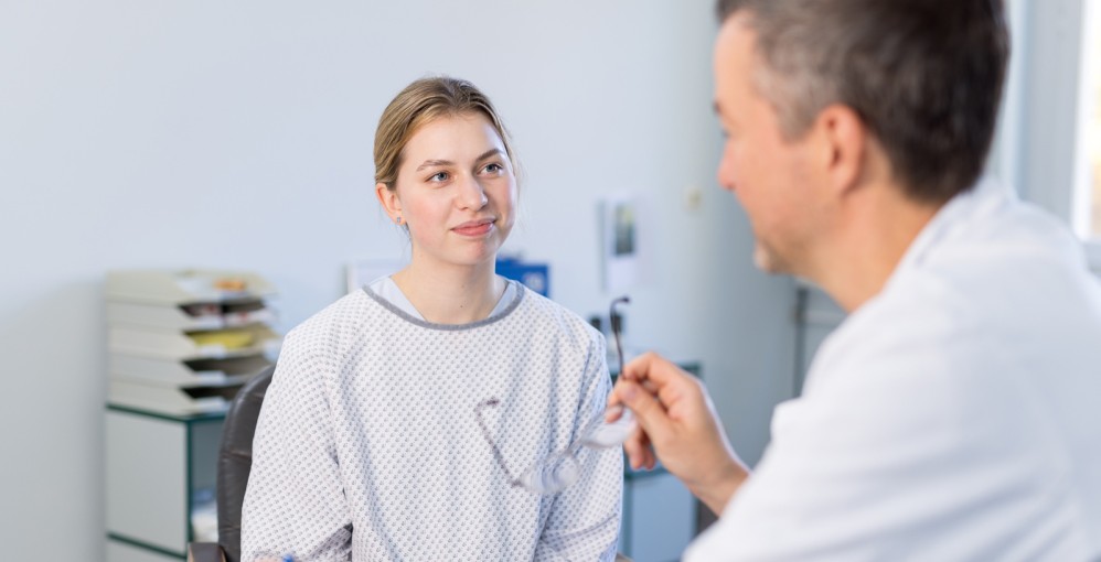 Eine junge Frau in einem OP-Oberteil sitzt vor einem Arzt, der ihr etwas erklärt.