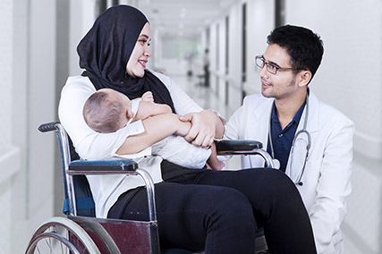 Eine Frau mit Baby sitzt im Rollstuhl und spricht mit einem Arzt.
