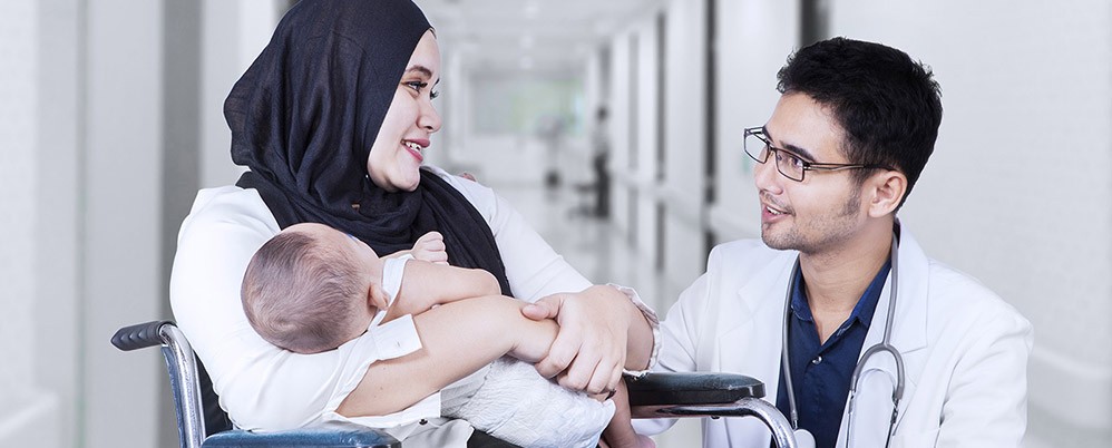 Eine Frau mit Baby sitzt im Rollstuhl und spricht mit einem Arzt.