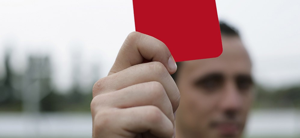 Das Bild zeigt einen Mann, der eine rote Karte hochhält.